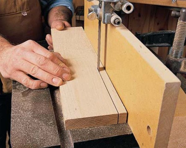 A man cutting a wood board with a bandsaw.
There is a fence very close to the inner side of the blade.
