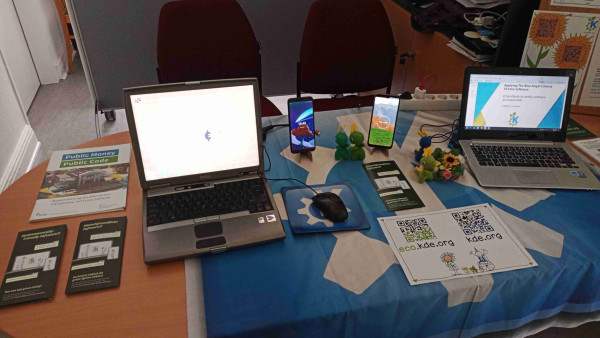 Image from KDE Eco's stand at the "Long Night Of The Sciences" at the German Environment Agency offices.

The computer on the left is 21 years old, running Haiku OS. An up-to-date version of GCompris was running on it, which children could play when coming to the booth.

The computer on the right is 11 years old, running Fedora KDE Spin. The PDF shown here is the KDE Eco handbook.

The left smartphone is a PinePhone running postmarketOS with Plasma-Mobile.

The right smartphone is a FairPhone 4 running Ubuntu Touch.

"Environmentally-Friendly Software" leaflets and amigurumi Konqi dolls are distributed around the table.

A KDE drop cloth can be seen on the table.