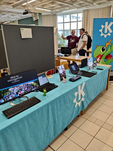 General view of KDE's booth at the event, showing a monitor displaying our "KDE for you" website, a laptop displaying Plasma, the Steam Deck games console, and the PinePhone running Plasma Mobile.